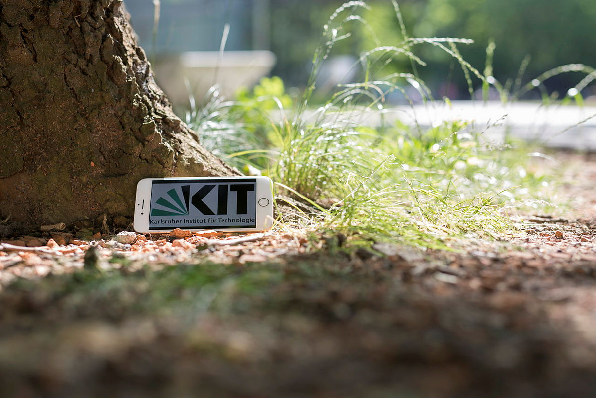 Handy mit KIT Logo auf dem Display unter einem Baum